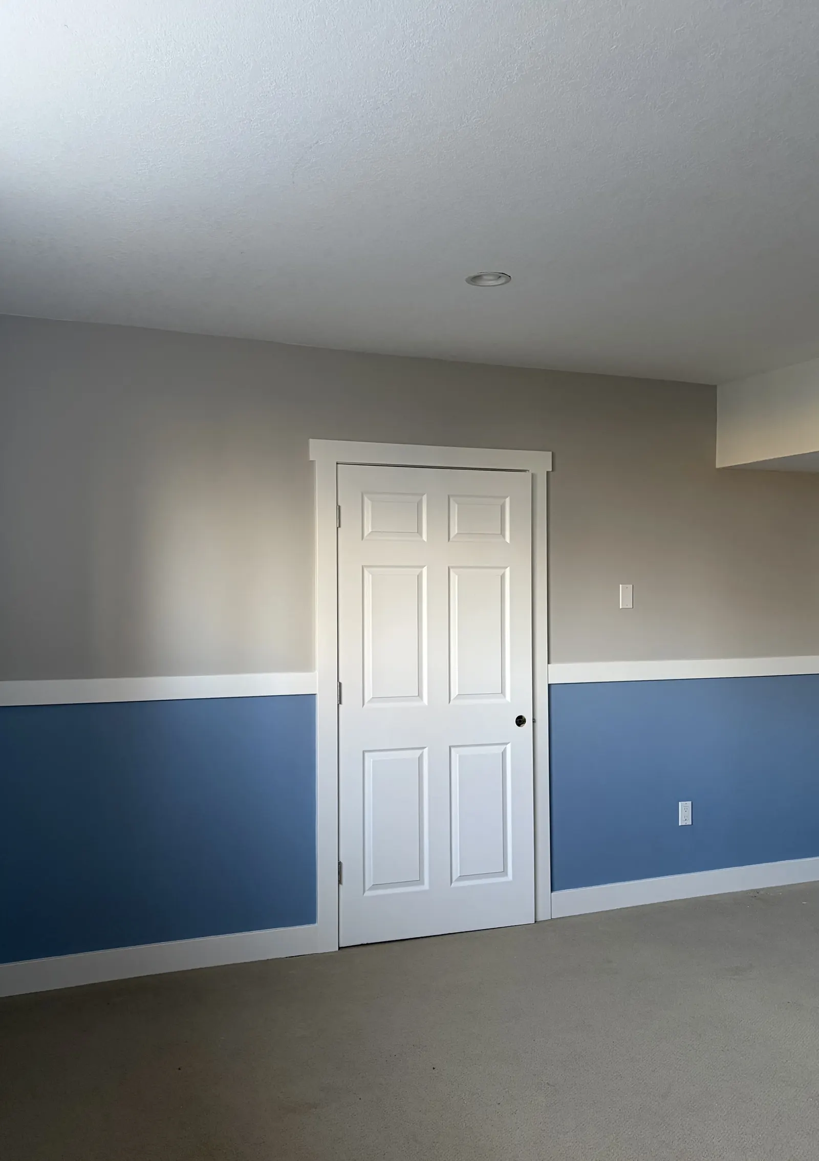 Basement wall after a smooth two-tone blue and tan finish with white door by Paint Pure