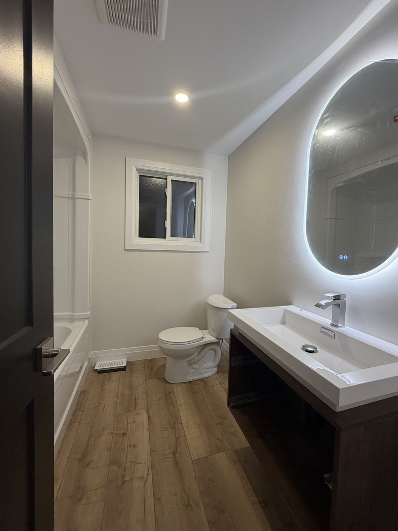 Newly finished bathroom with a backlit LED mirror and wood-look flooring painted by Paint Pure