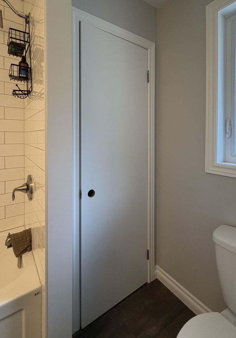 Grey bathroom with a clean white pocket door and subway-tile shower painted by Paint Pure