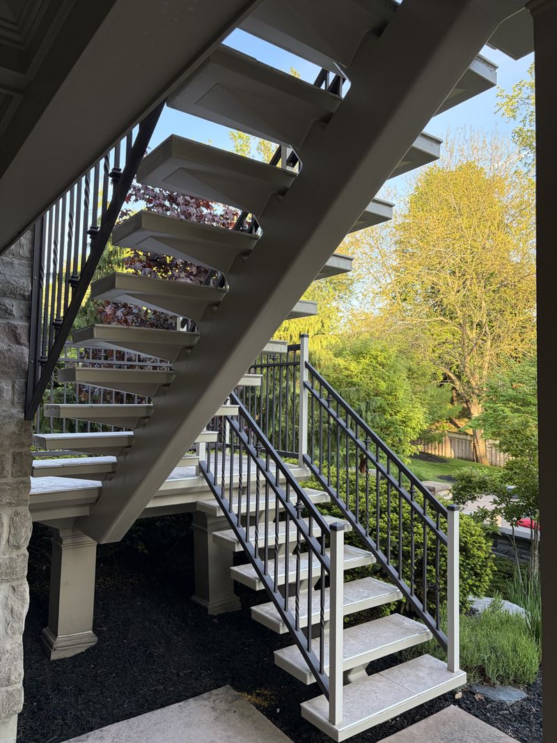 Freshly painted backyard deck staircase with black metal railings at golden hour by Paint Pure