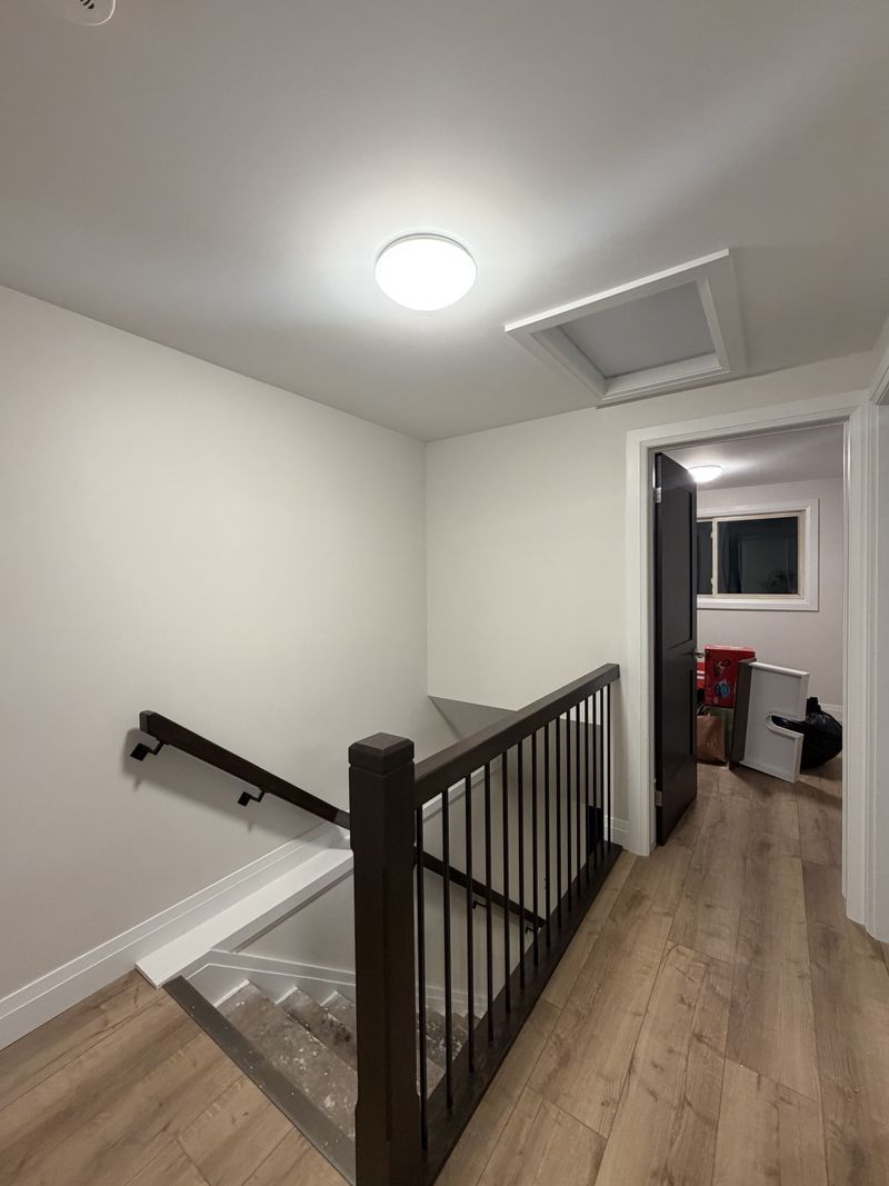 Clean white stair landing with a black railing and wood-look floors painted by Paint Pure