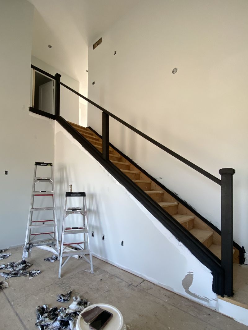 Tall stairwell with a freshly painted black railing against bright white walls by Paint Pure